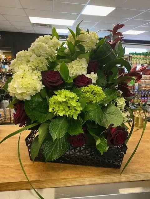 A beautiful custom floral arrangement from Pawtuxet Village Market featuring white hydrangeas and deep red roses in an elegant black basket.