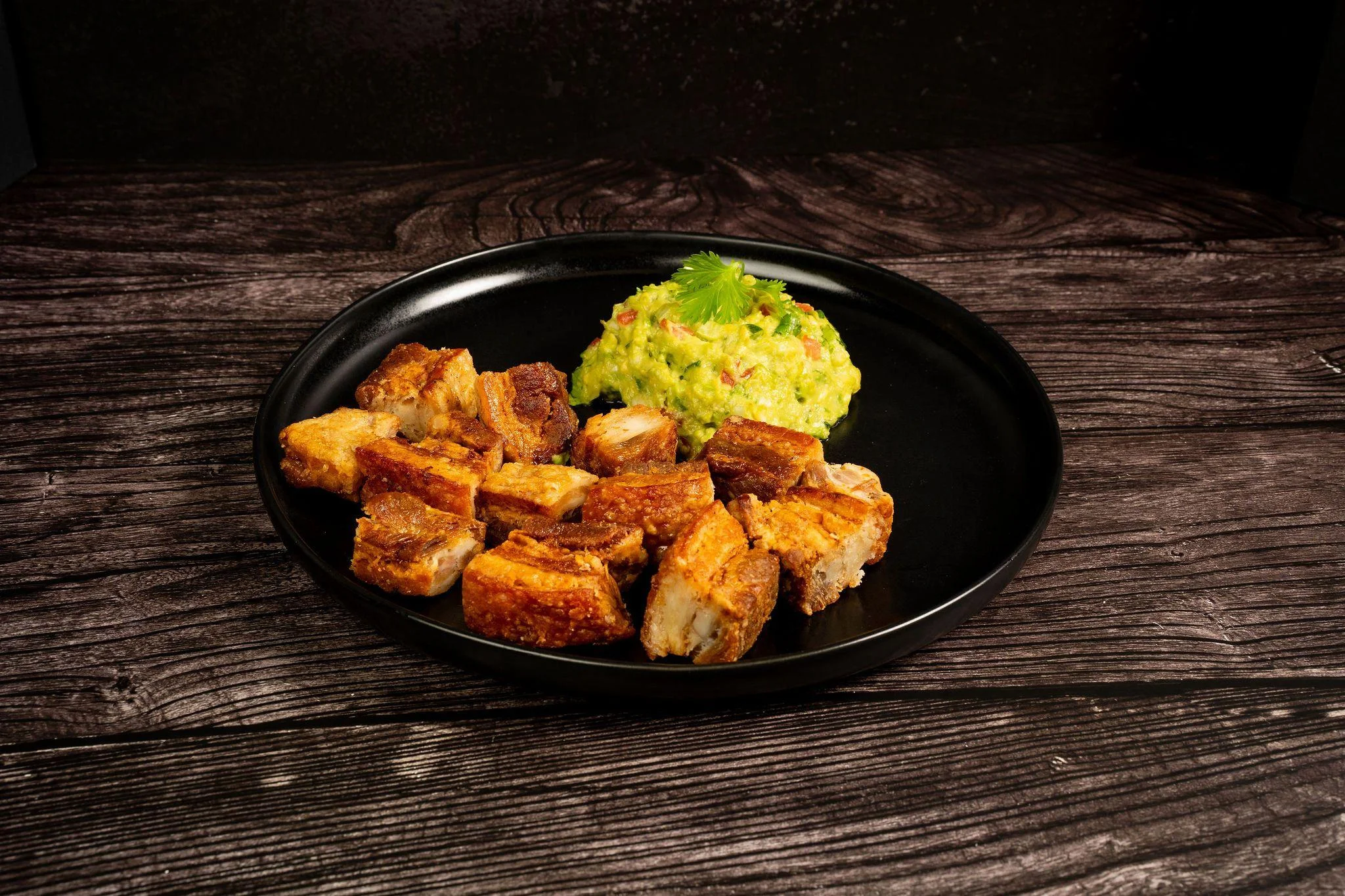 Crispy chunks of roasted pork served alongside a portion of guacamole garnished with herbs.