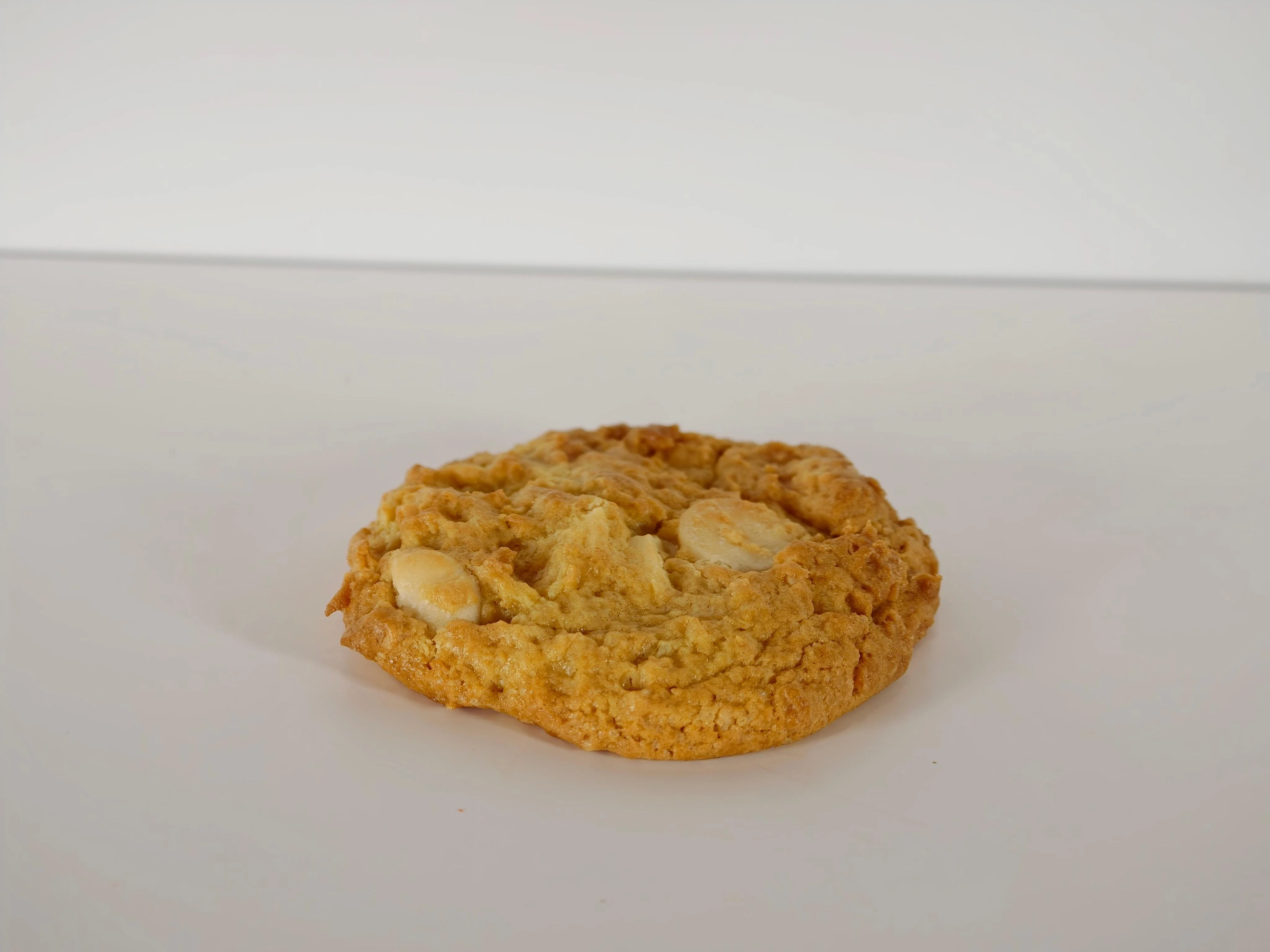A single large cookie with a golden-brown color and visible chunks of white ingredients.