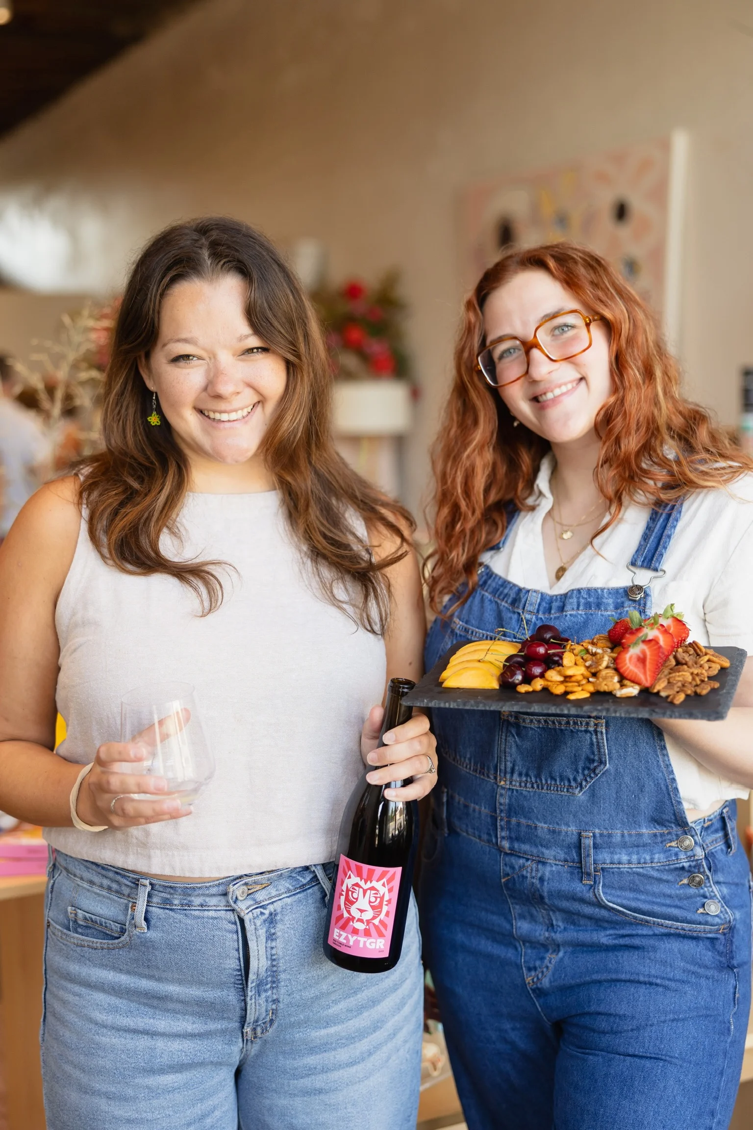 Two women holding wine and a charcuterie board in a vibrant setting