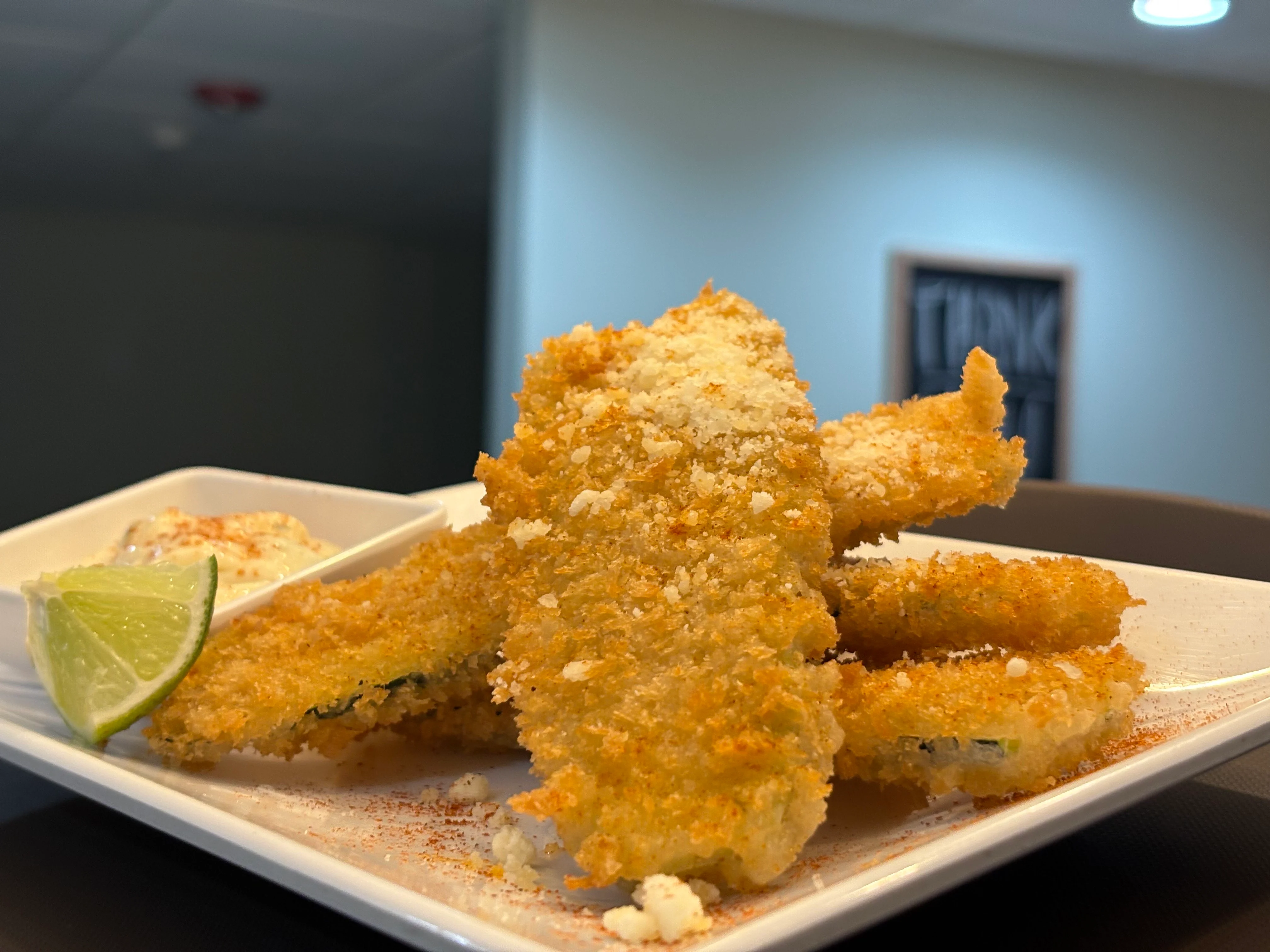 Crispy fried zucchini sticks served with a lime wedge and a creamy dipping sauce.