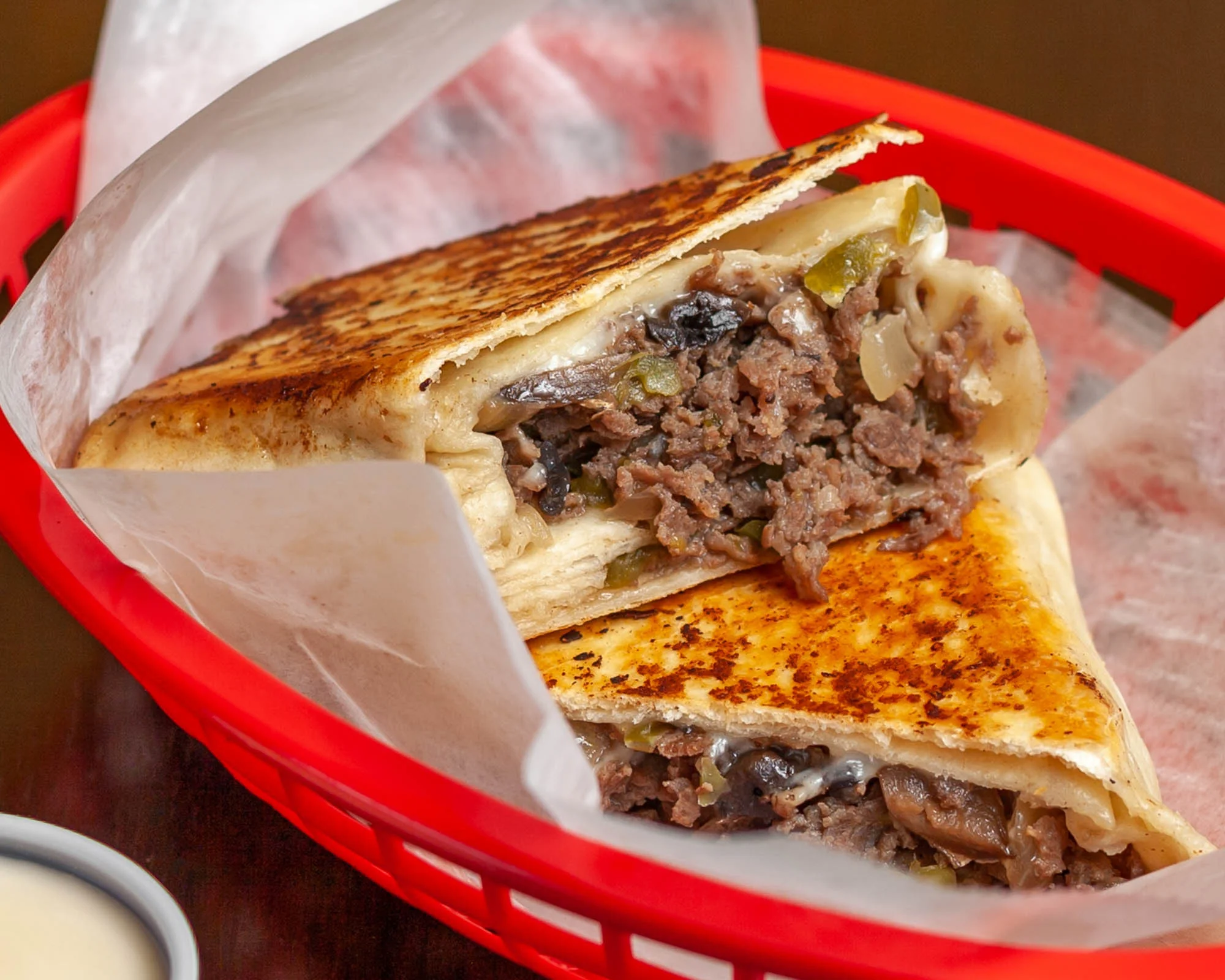A two-part grilled quesadilla filled with beef and vegetables, served in a red basket with some parchment paper.