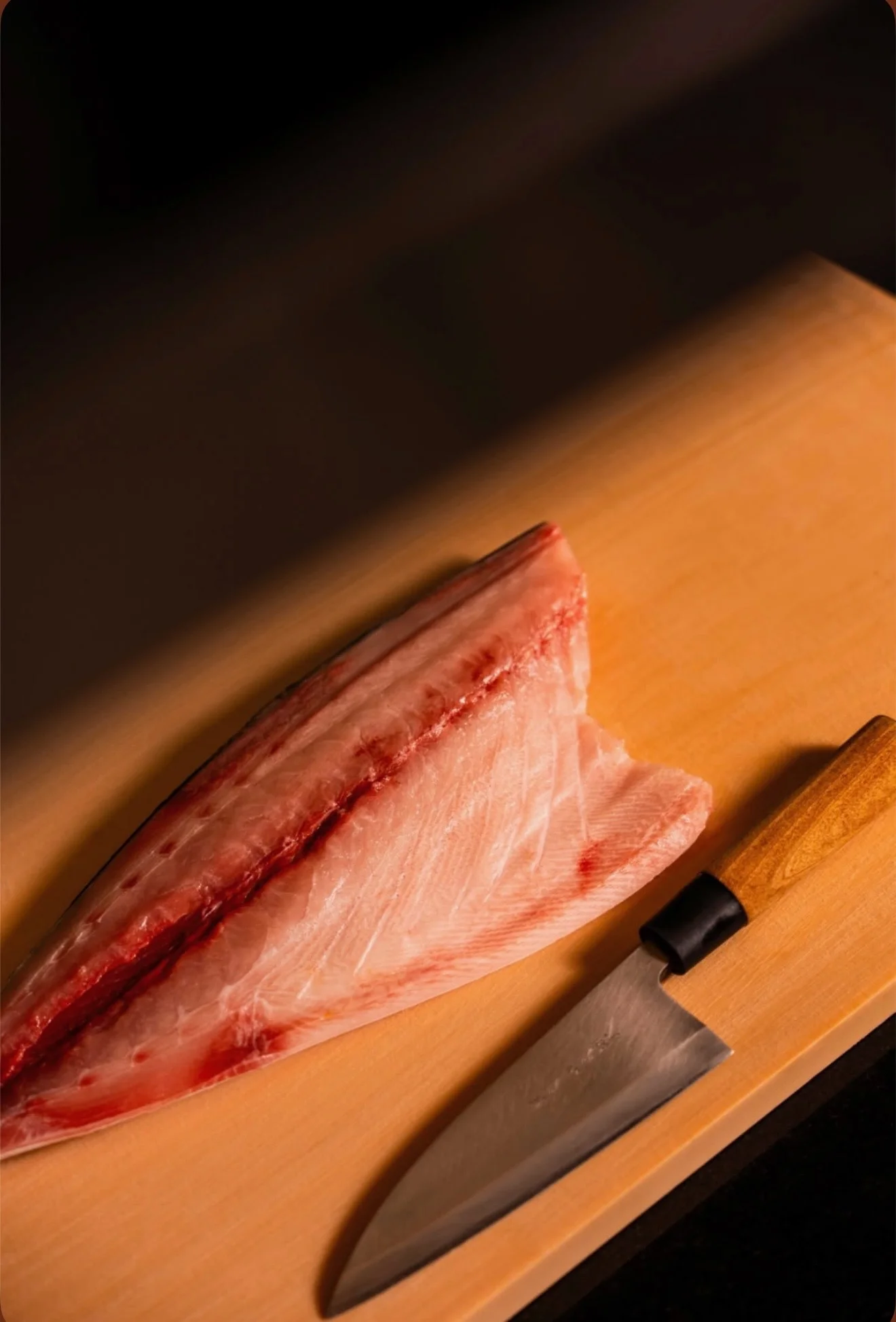 Sliced fish fillet with a traditional Japanese knife on a wooden board