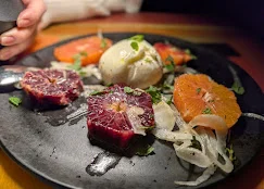 A black plate featuring colorful citrus sections, creamy burrata, and thinly sliced onions. Fresh mint adds a pop of green.
