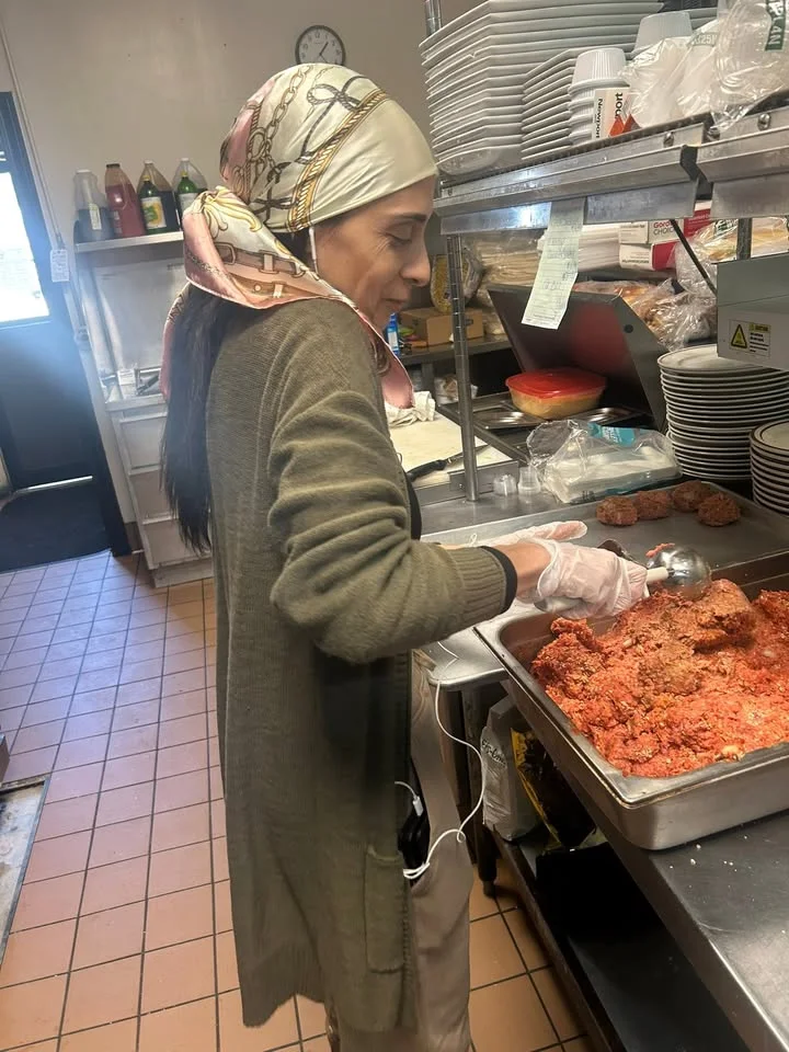 A person in a kitchen preparing food. They are scooping a mixture from a pan while wearing gloves.