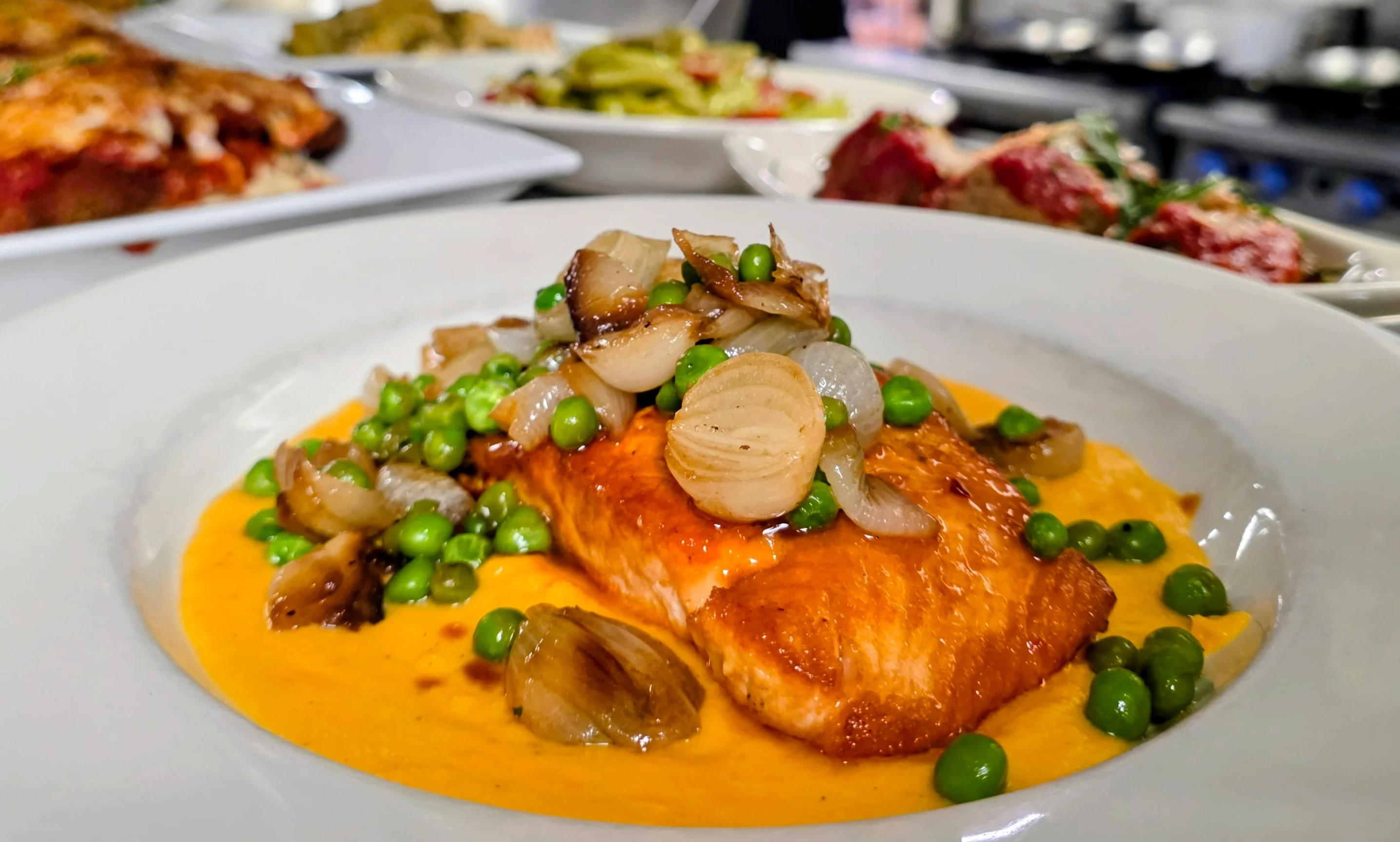 Pan-seared salmon with creamy sauce in a bustling restaurant kitchen