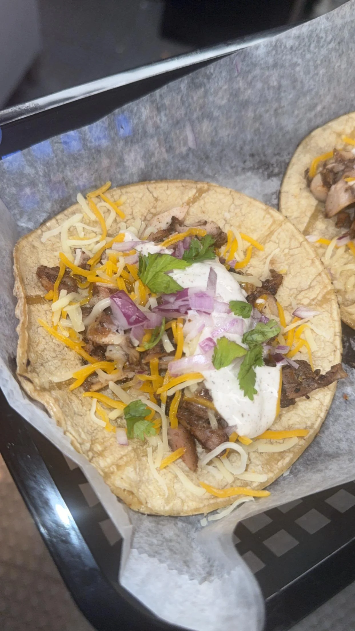 Tacos filled with grilled meat, topped with cheese, onions, and a drizzle of sauce, served in a corn tortilla.