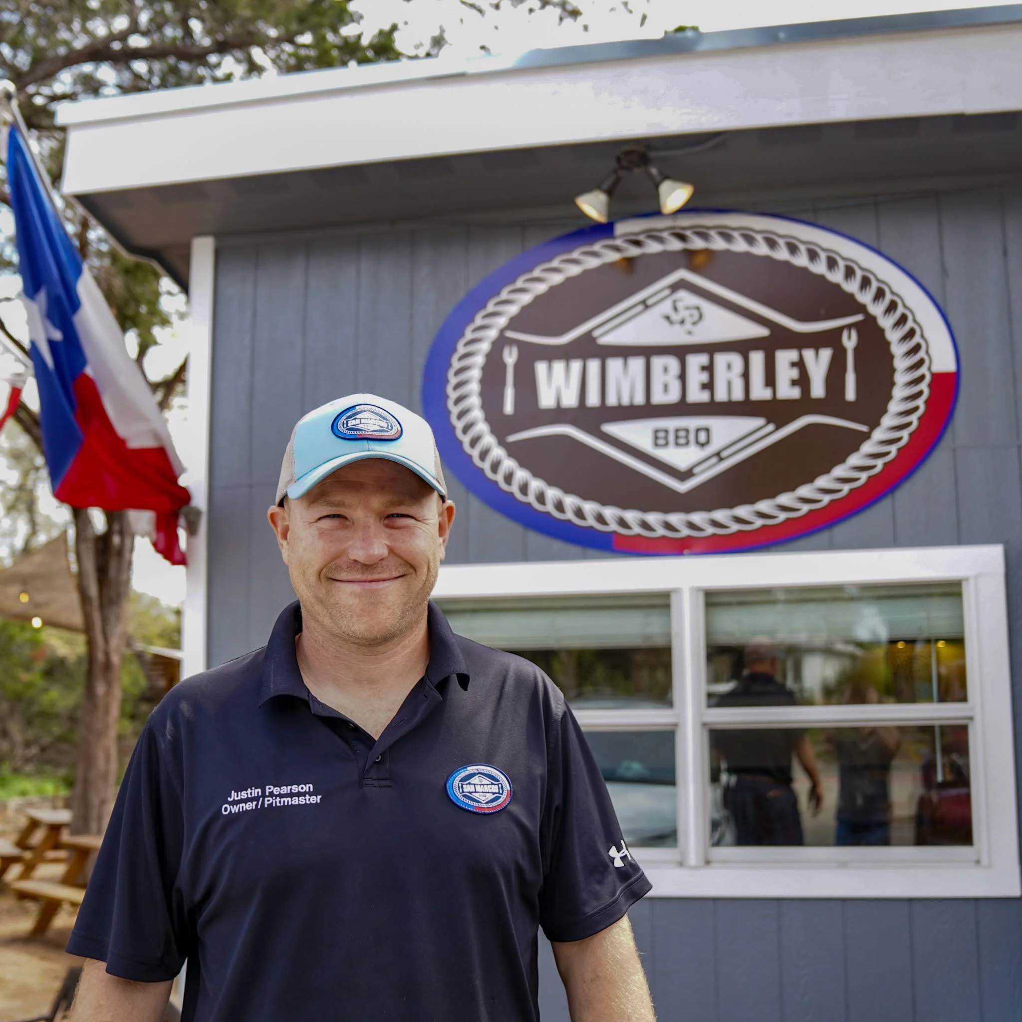 Owner of Wimberley BBQ in front of restaurant signage