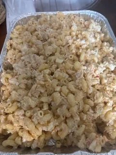 A large tray filled with creamy macaroni salad, featuring small pasta mixed with a mayonnaise-based dressing and chunks of chicken or seafood.