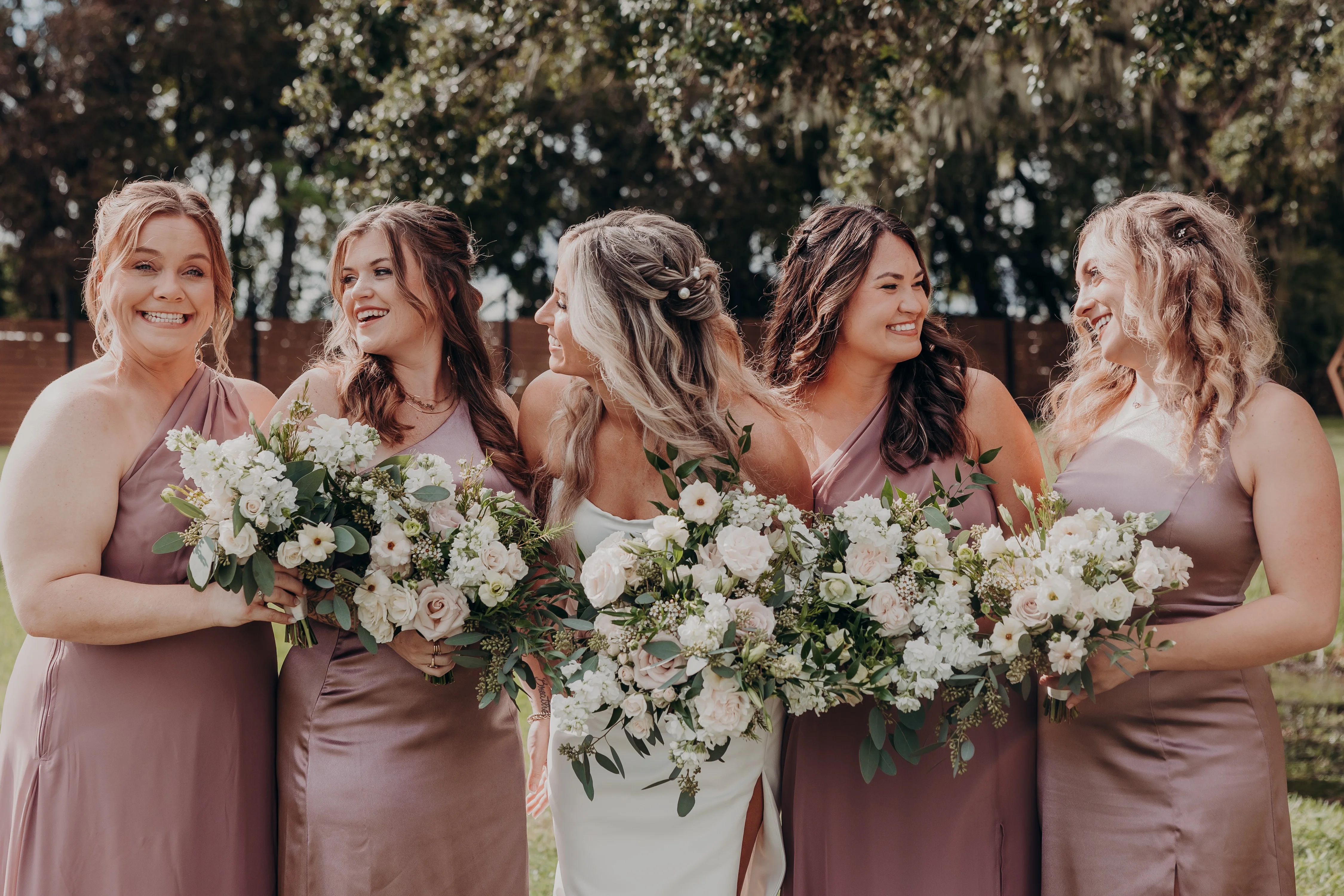 Bridesmaids smiling with floral bouquets in a sunny outdoor setting