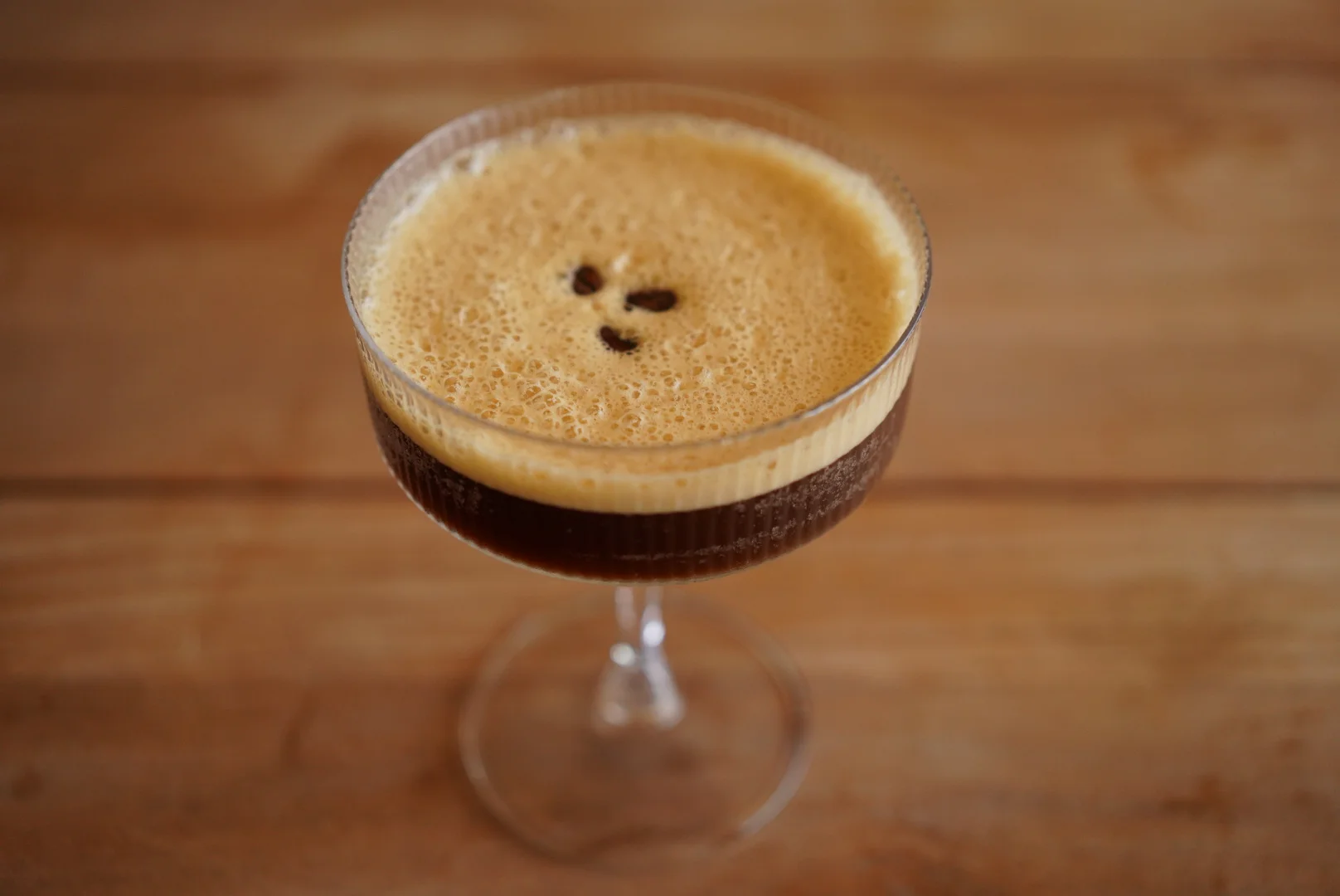 A close-up of a frothy dark cocktail served in a stemmed glass, showcasing its creamy layer and bubbles.