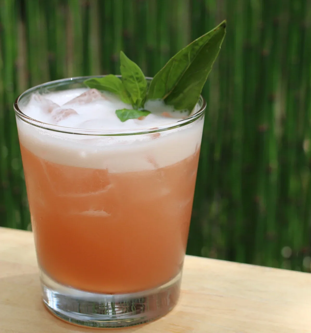 Colorful cocktail garnished with fruit and herbs on a wooden table.