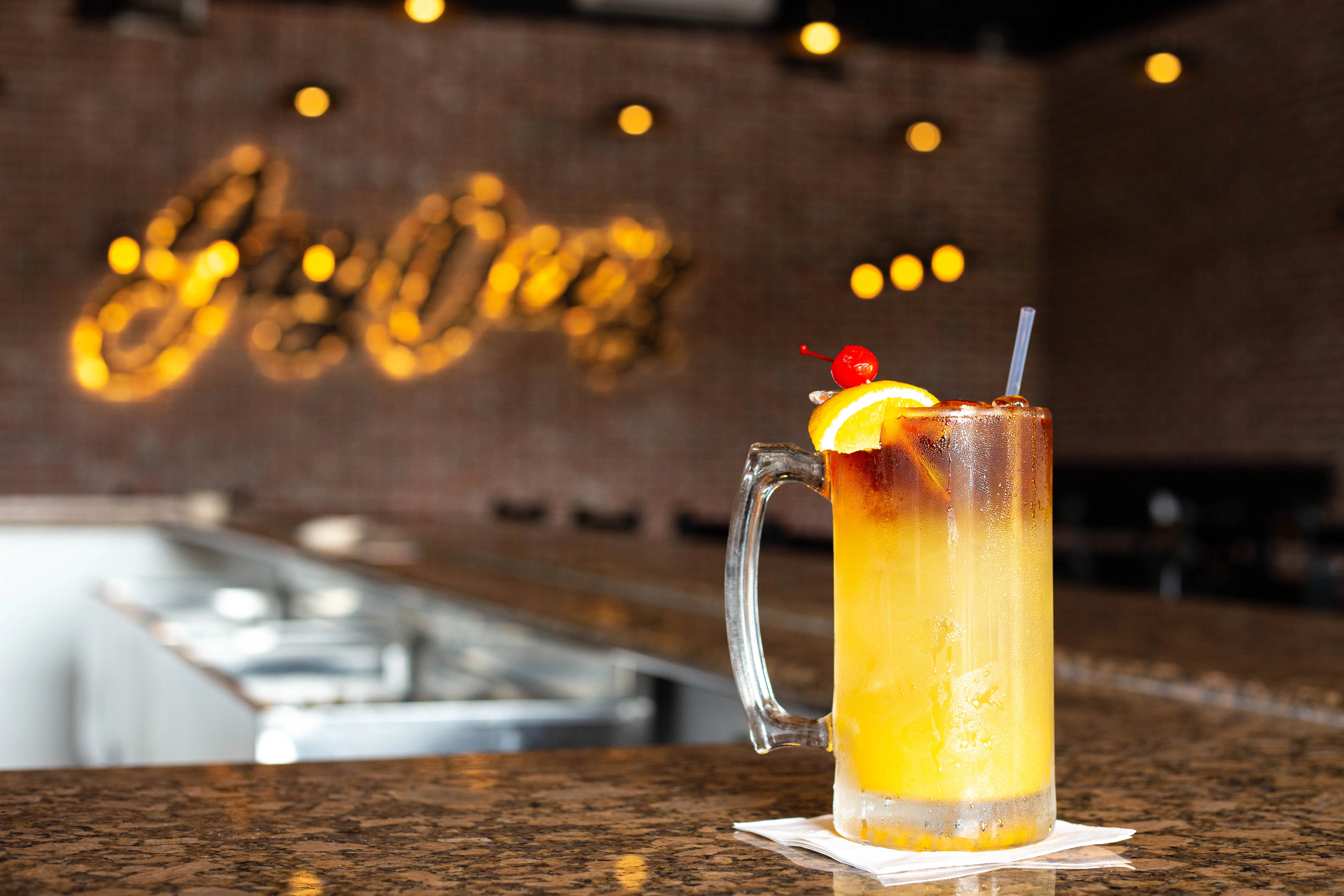A refreshing cocktail in a glass mug garnished with a slice of orange and a cherry, sitting on a granite countertop.