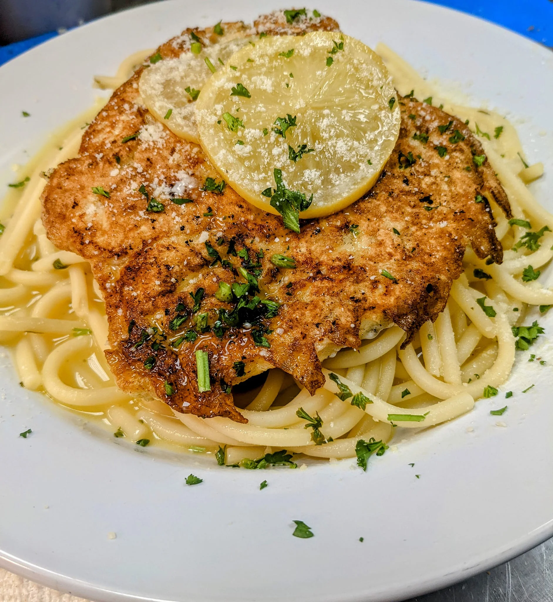 A plate of linguine topped with a seasoned fish fillet and garnished with lemon slices and parsley.