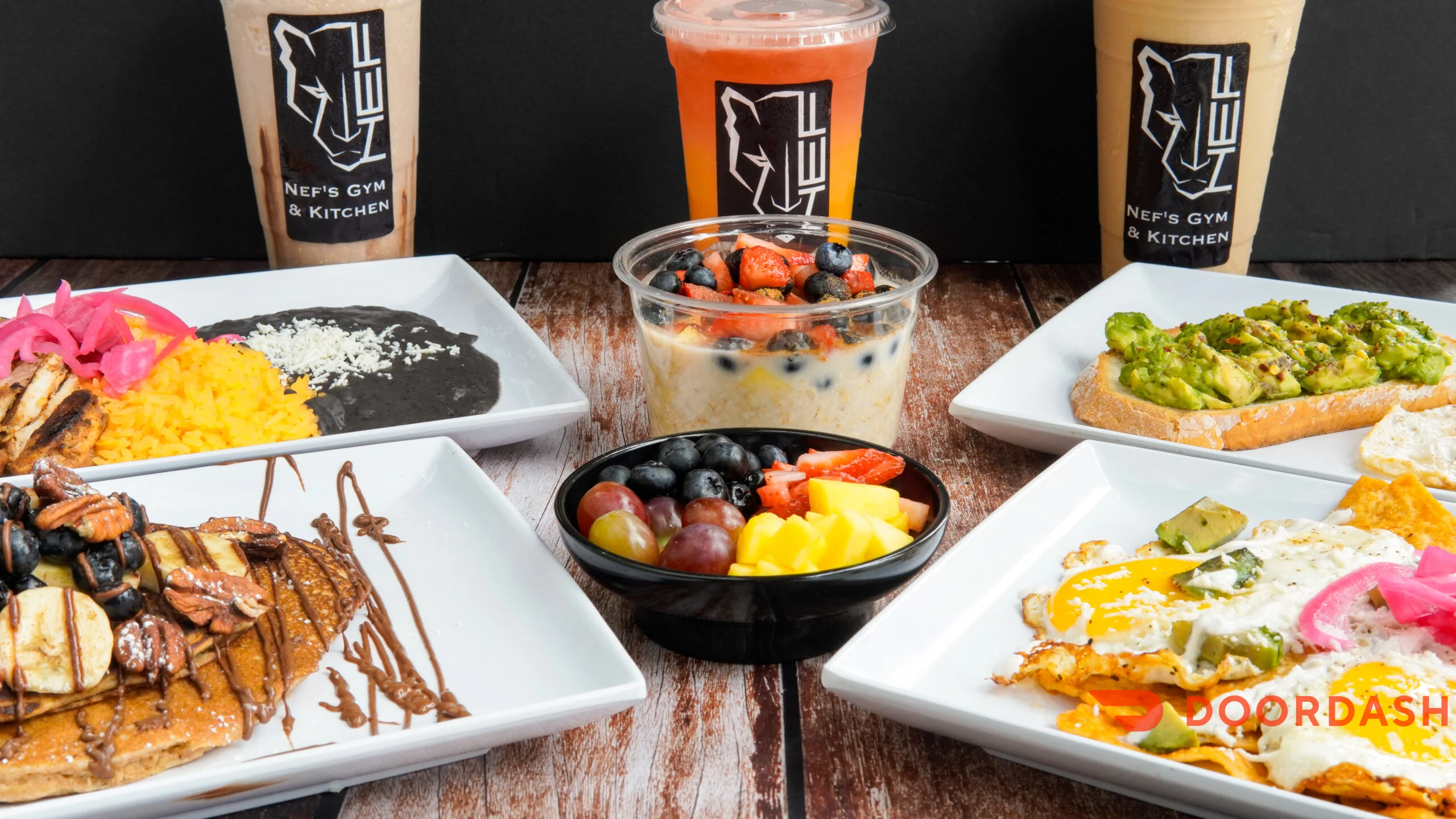 A variety of dishes and drinks arranged on a table, including pancakes, rice, vegetables, fruit, and smoothies, all served in modern white plates.