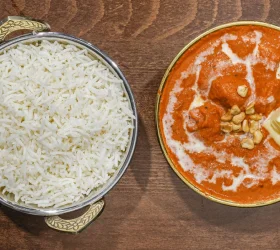 A serving of butter chicken accompanied by fluffy white rice, garnished with cashews.