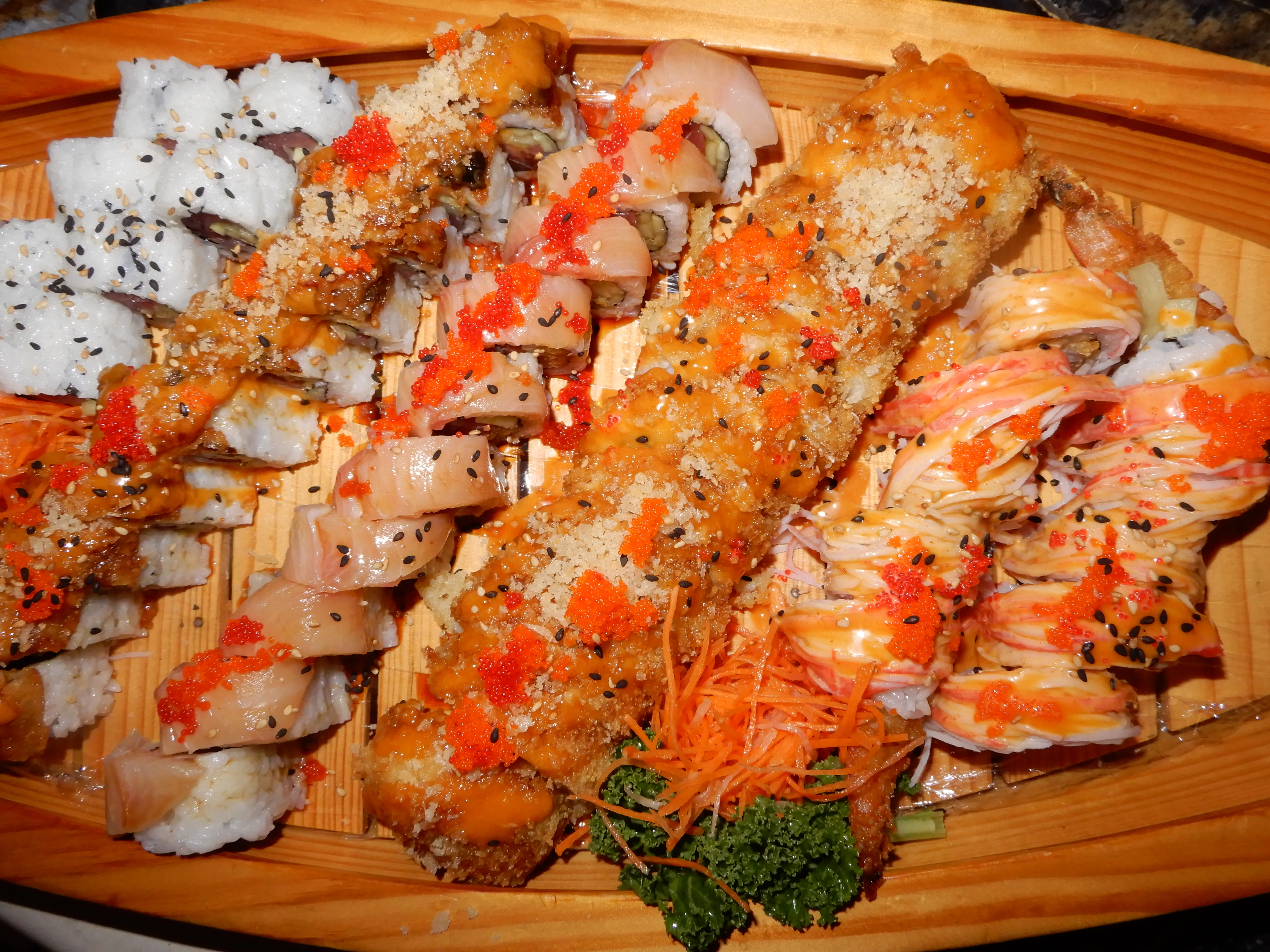 A cartoon character wearing a chef's outfit is giving a thumbs-up while holding a tray of sushi. The background features a circular red design with the restaurant's name 'TASIA' displayed prominently below.