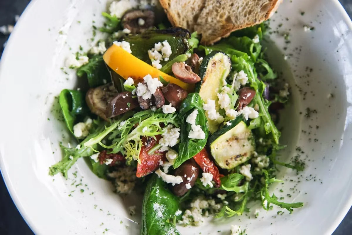 Colorful salad with greens, grilled vegetables, olives, and bread.