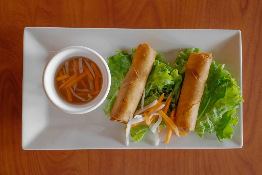 Two spring rolls served on a bed of lettuce with a small dipping sauce, accompanied by shredded vegetables.