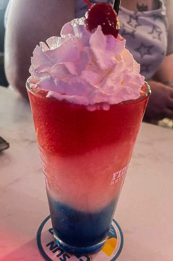 Colorful layered cocktail with whipped cream and cherry