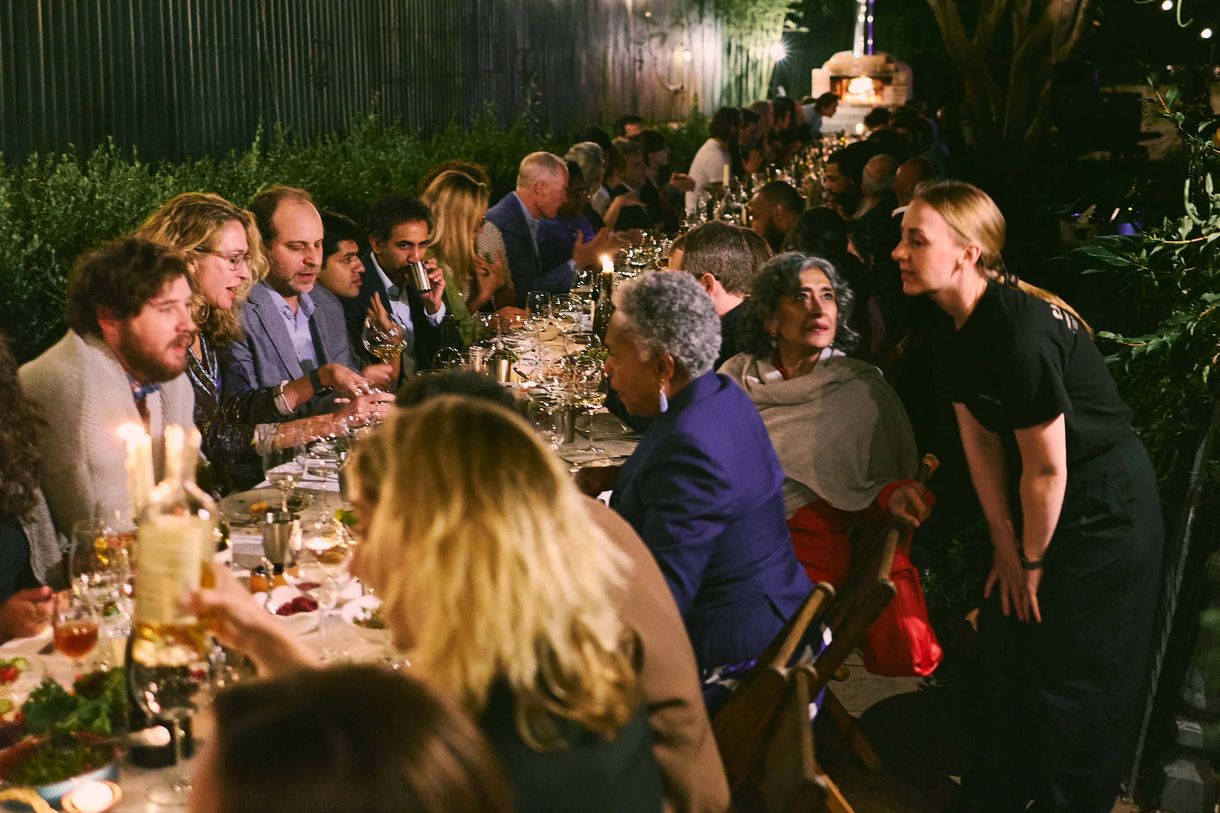 Outdoor restaurant dinner with guests gathered around a candlelit communal table