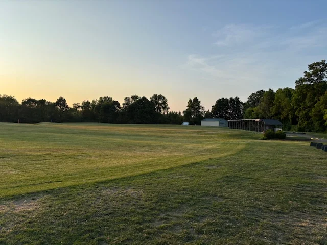 Open field at sunset with trees and a building in the background