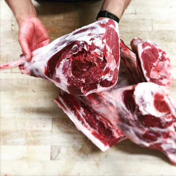 A person holding a large piece of raw meat, showcasing its detailed texture and cut, with additional cuts of meat in the background.