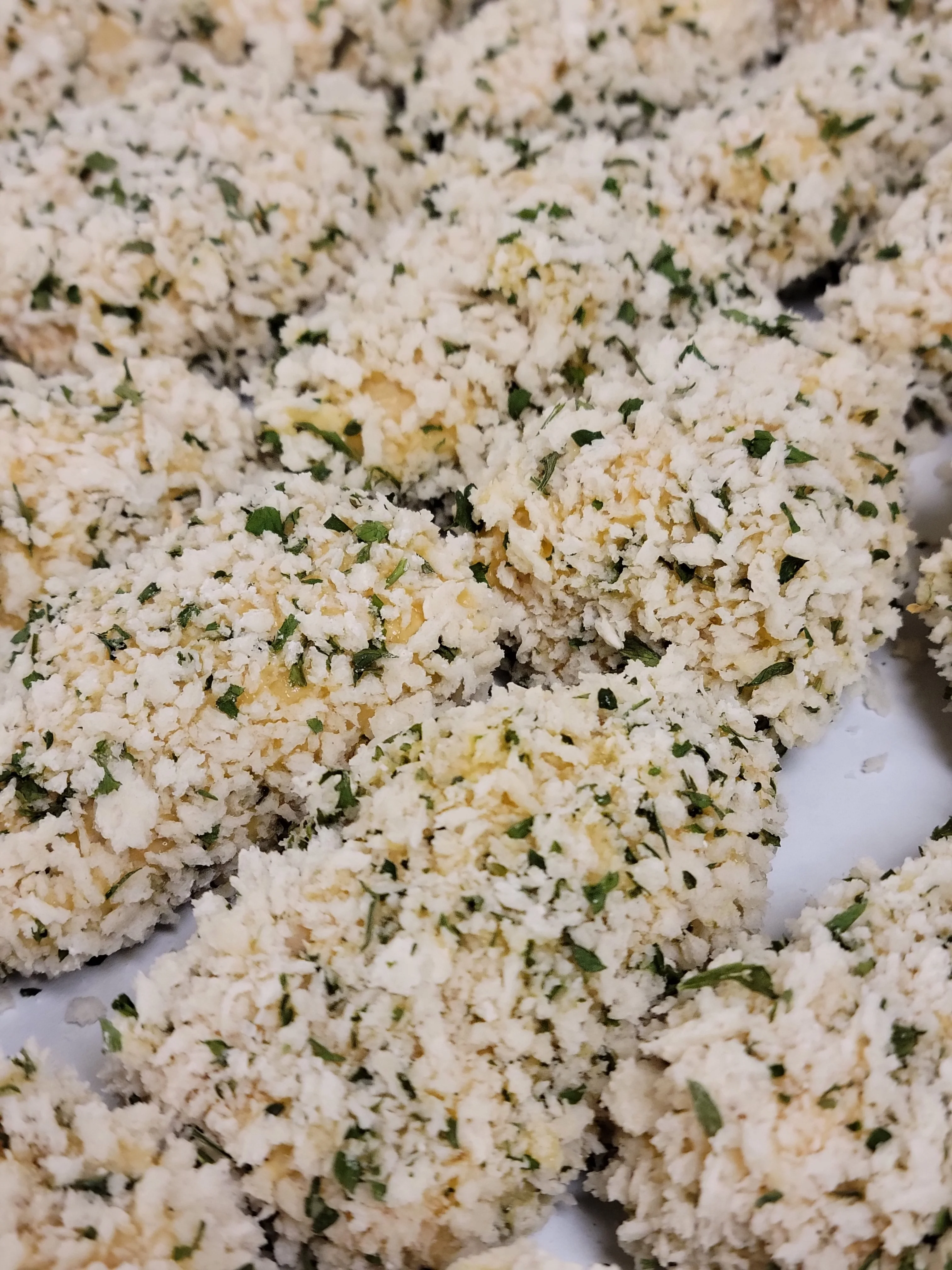 A close-up view of breaded and herb-coated food items, arranged neatly with a textured appearance.