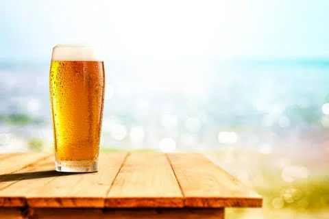 Chilled glass of beer on a wooden table by the beach
