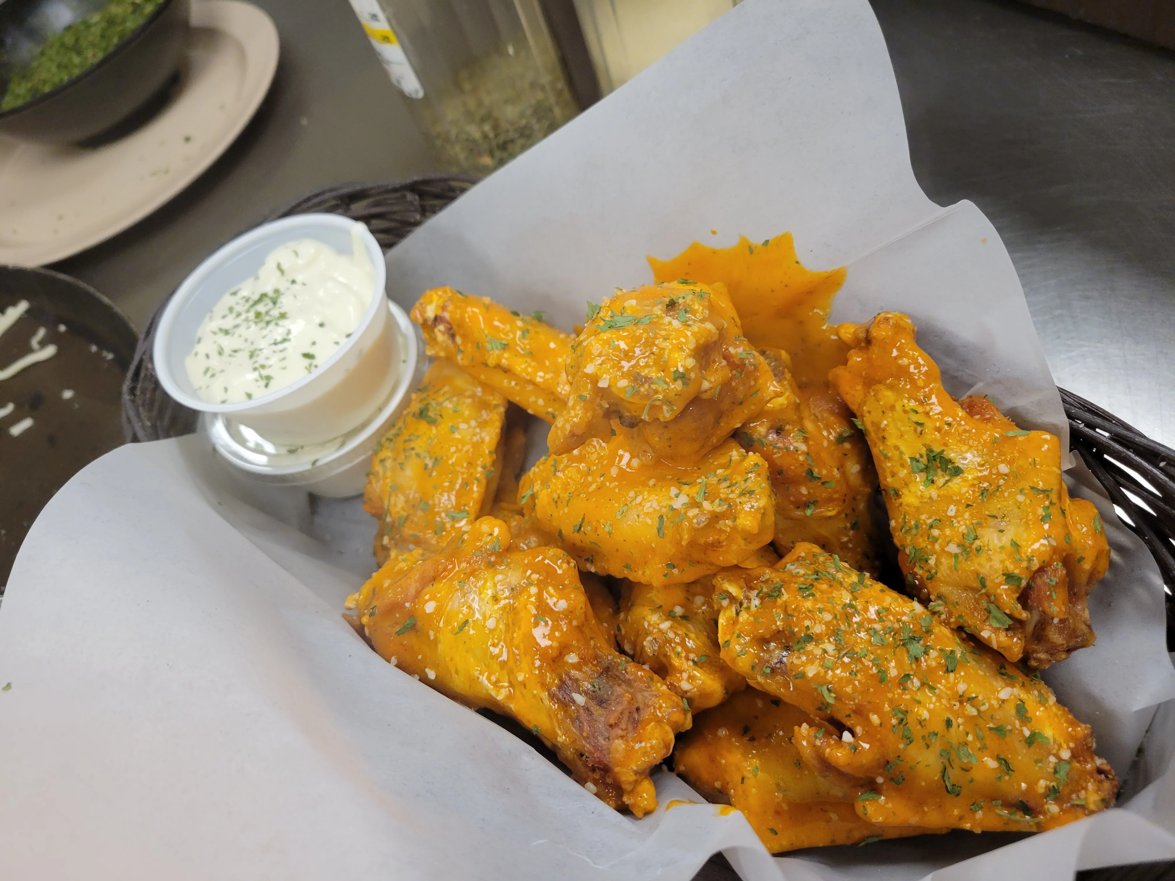 A serving of golden chicken wings garnished with herbs, accompanied by a small container of dipping sauce.