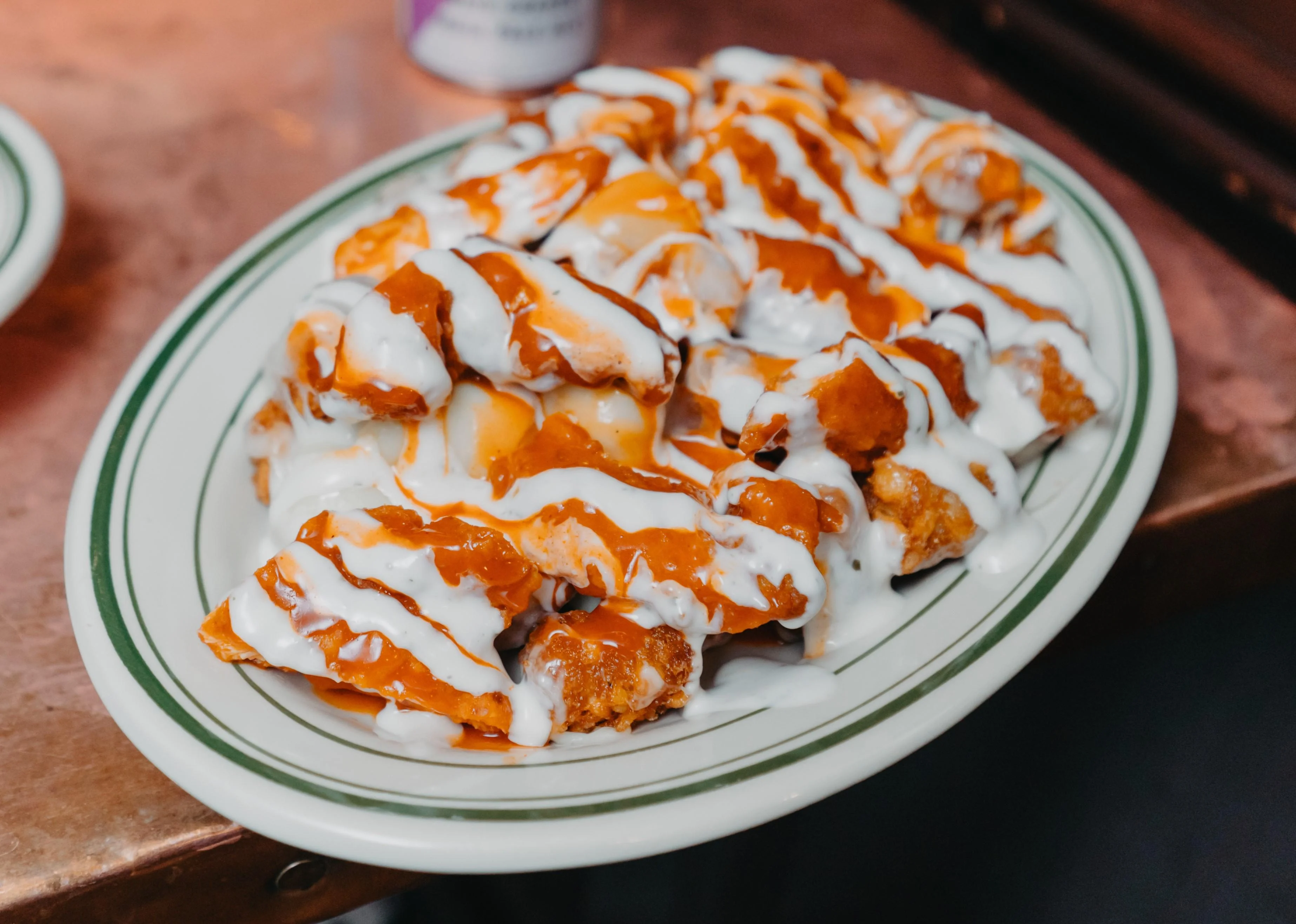 A platter of crispy chicken pieces drizzled with a creamy sauce and a spicy sauce, layered artistically on a white plate.