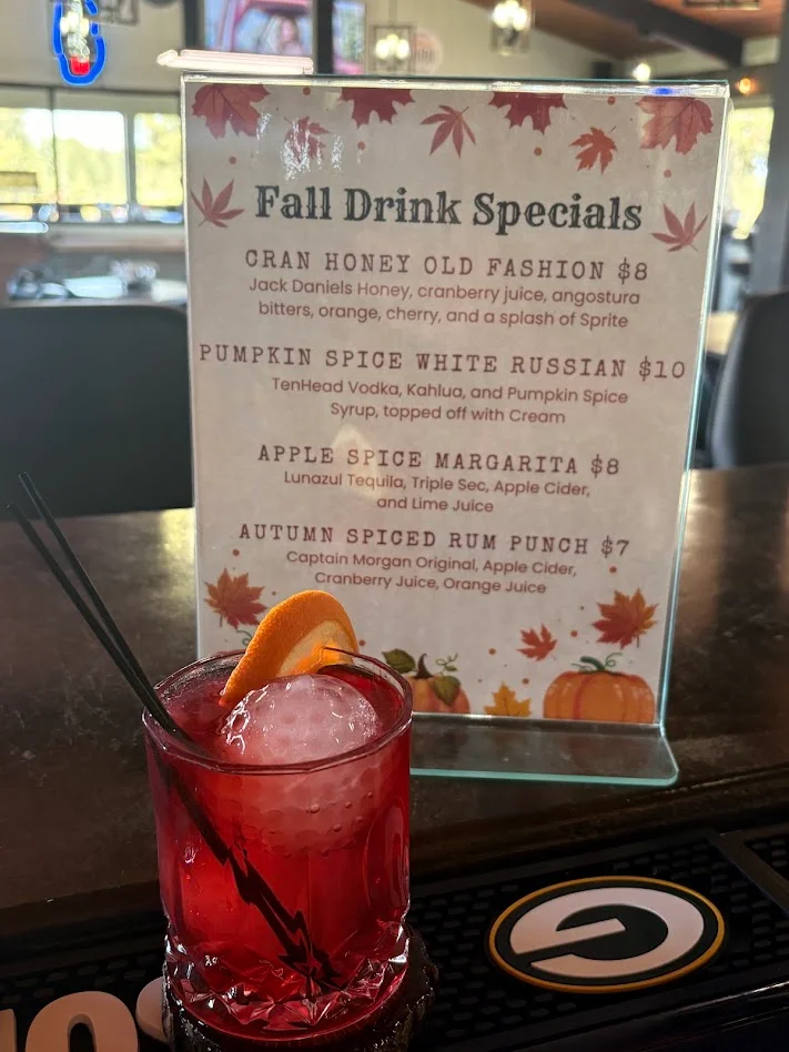 Red seasonal cocktail with orange garnish beside fall drink specials menu