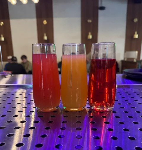 Three colorful drinks in shot glasses on a metallic surface.
