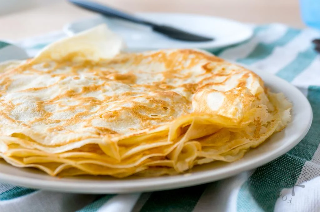 A stack of thin, golden crepes neatly arranged on a plate.