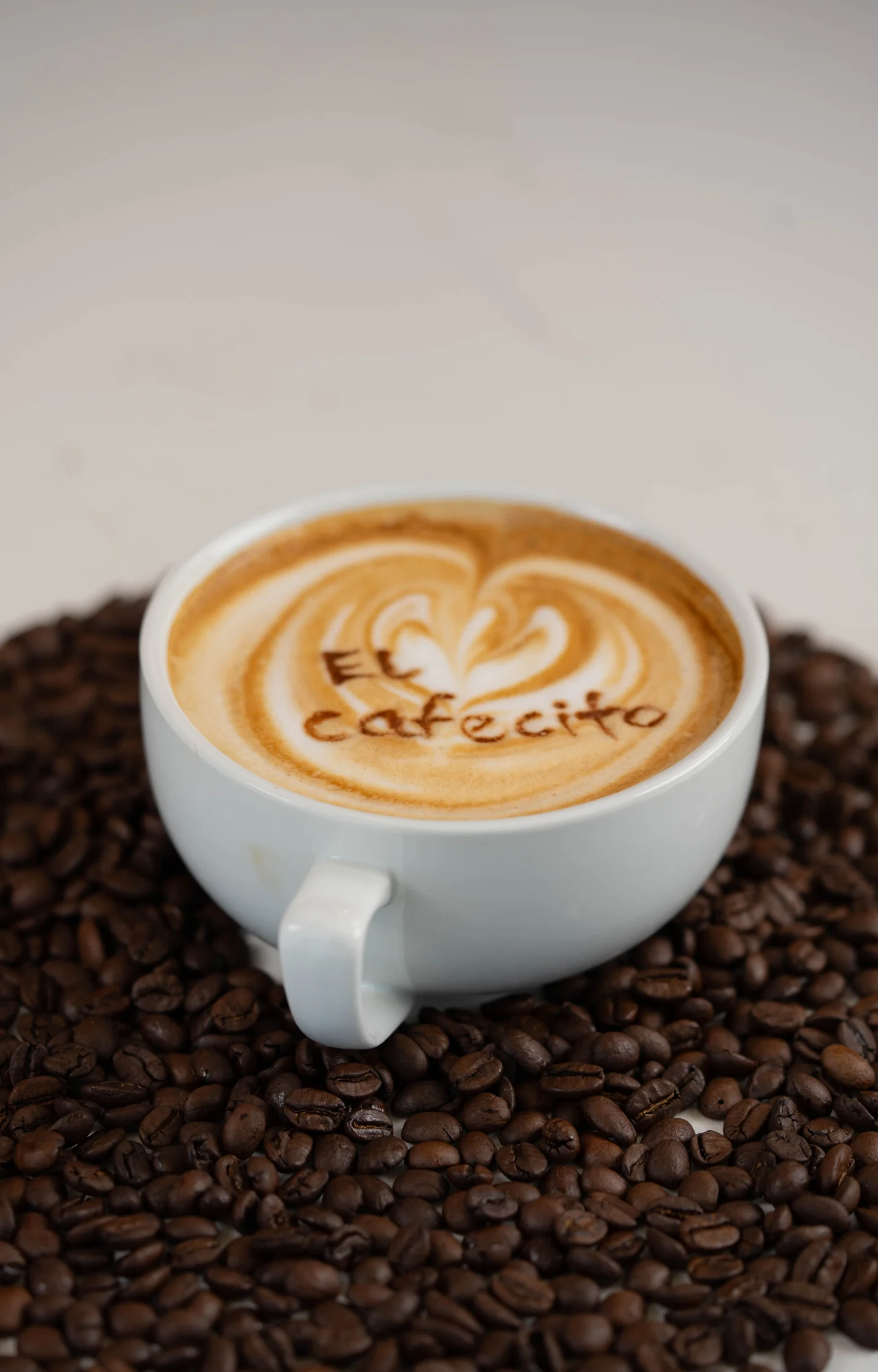 A latte with 'El Cafecito' art on top, surrounded by coffee beans.