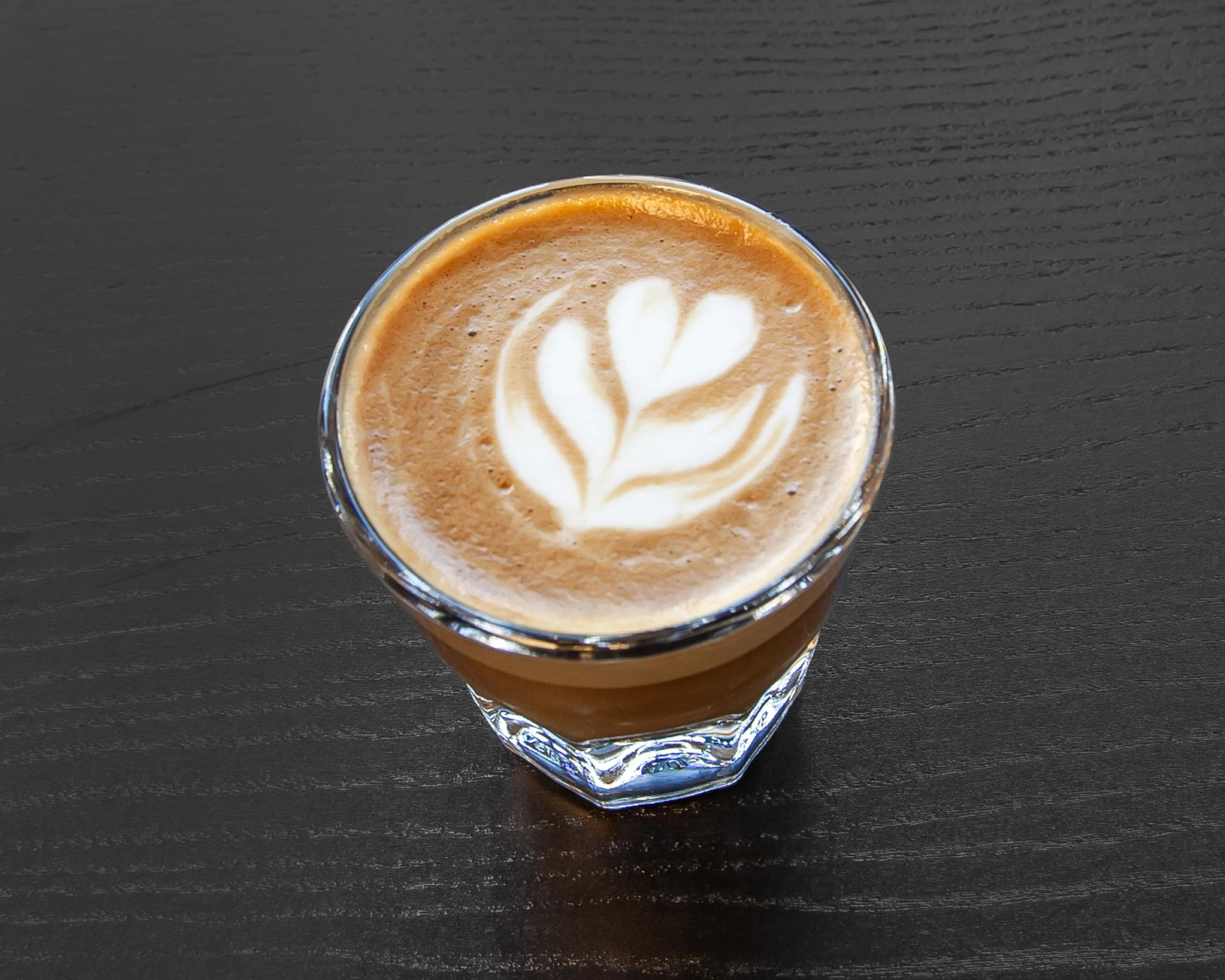A creamy coffee drink served in a glass, garnished with coffee-based latte art.