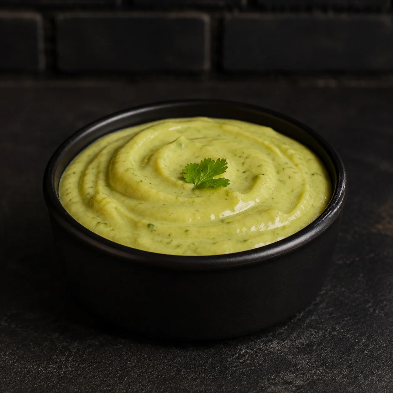 Creamy avocado sauce in a black bowl, garnished with cilantro