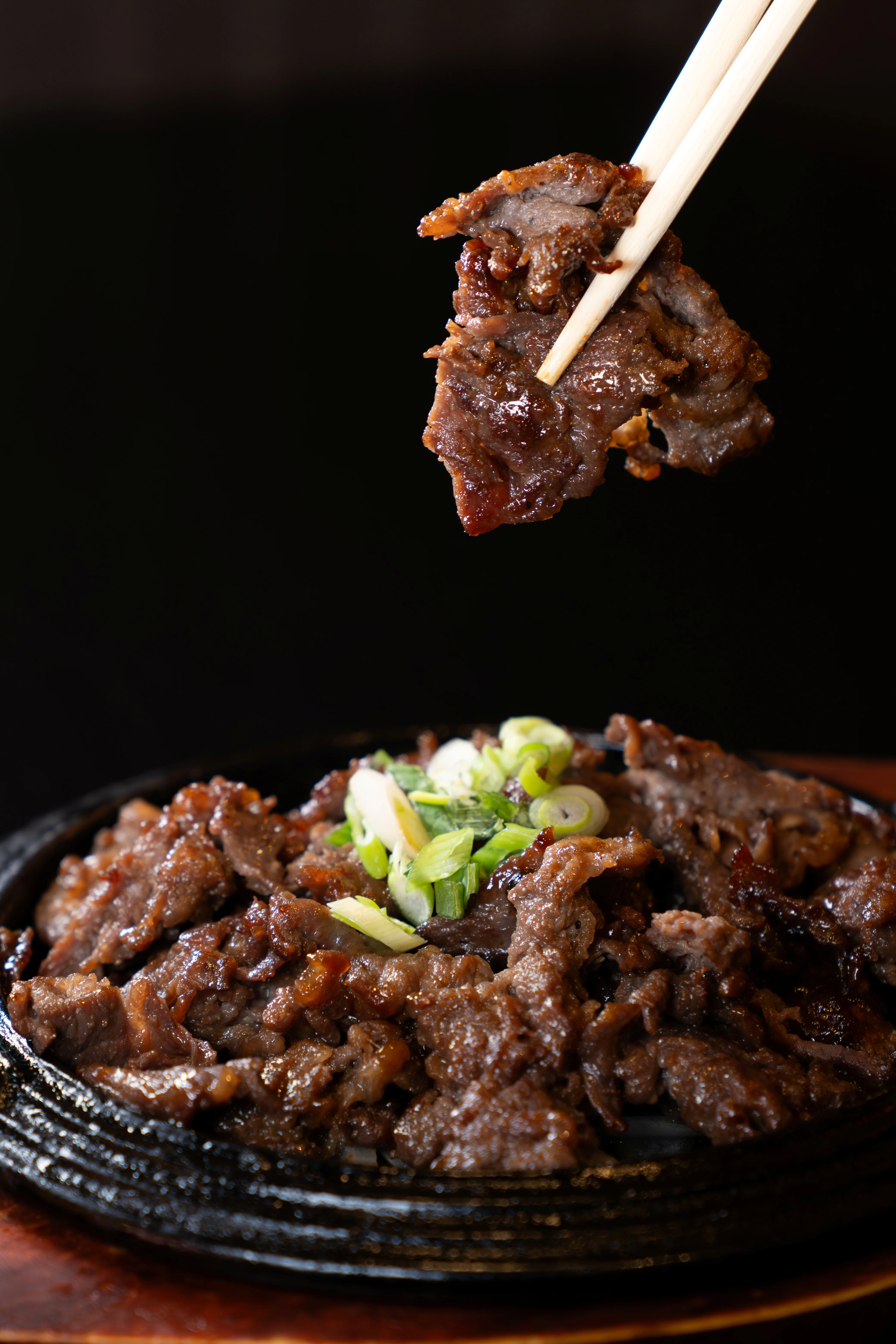 Sizzling beef dish with green onions served on a hot plate.