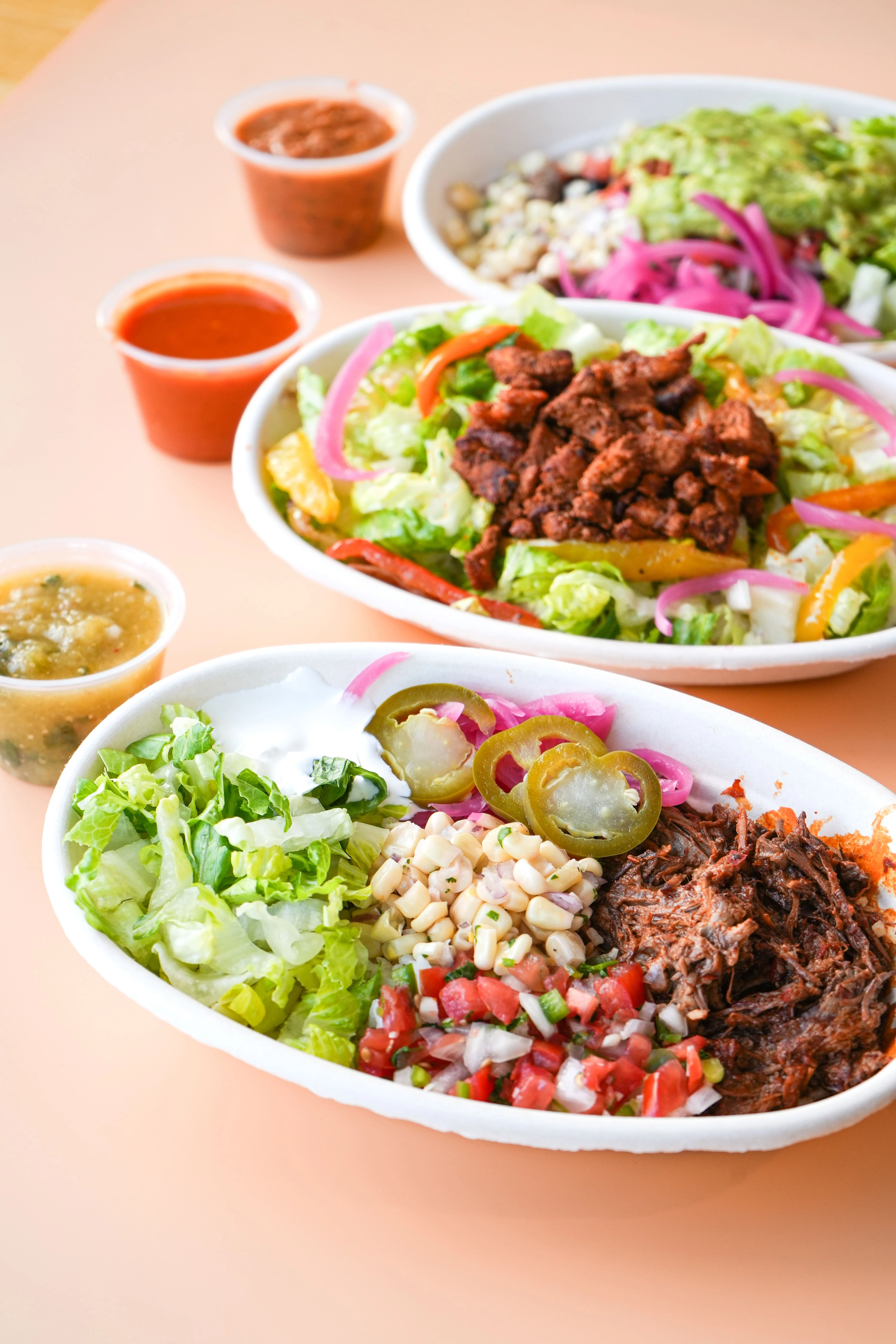 Two bowls with a variety of fresh ingredients including lettuce, meats, vegetables, and sauces, served alongside additional sauce containers.