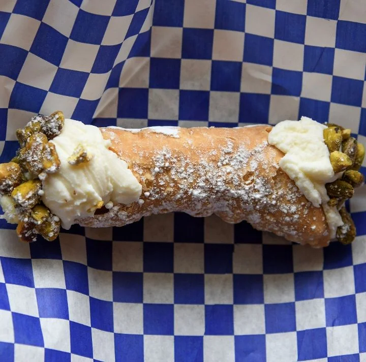 A delicious cannoli filled with cream and topped with pistachios, served on a checkered paper.