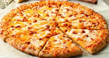 A round pizza with a golden crust, topped with melted cheese and pieces of chicken, sliced into eight segments.