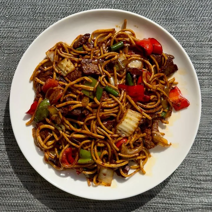Beef chow mein with colorful vegetables on a white plate