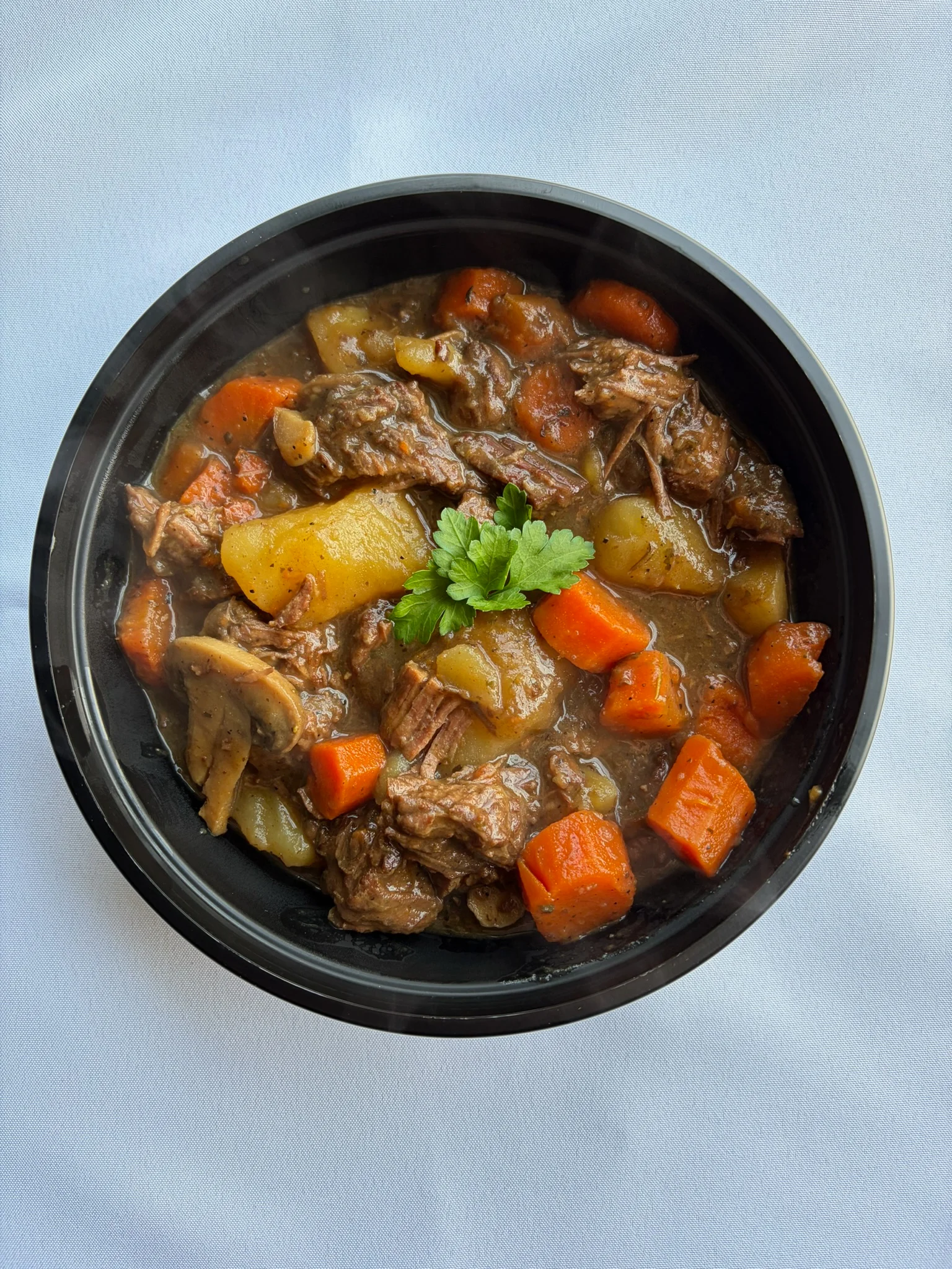 Hearty beef stew with vegetables in a black bowl