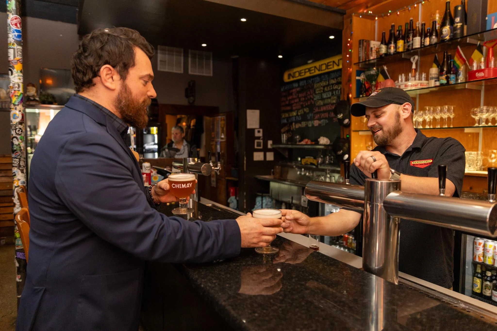 Bartender serving Chimay beer at a lively bar counter