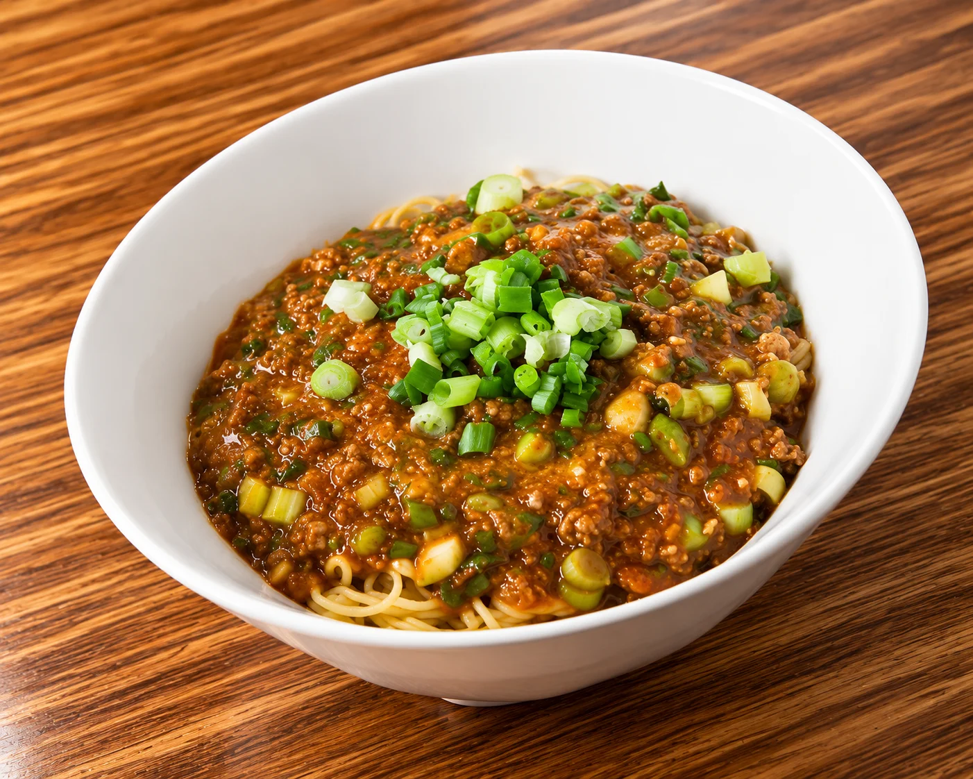 Bowl of spicy noodles topped with savory minced meat sauce and chopped green onions.