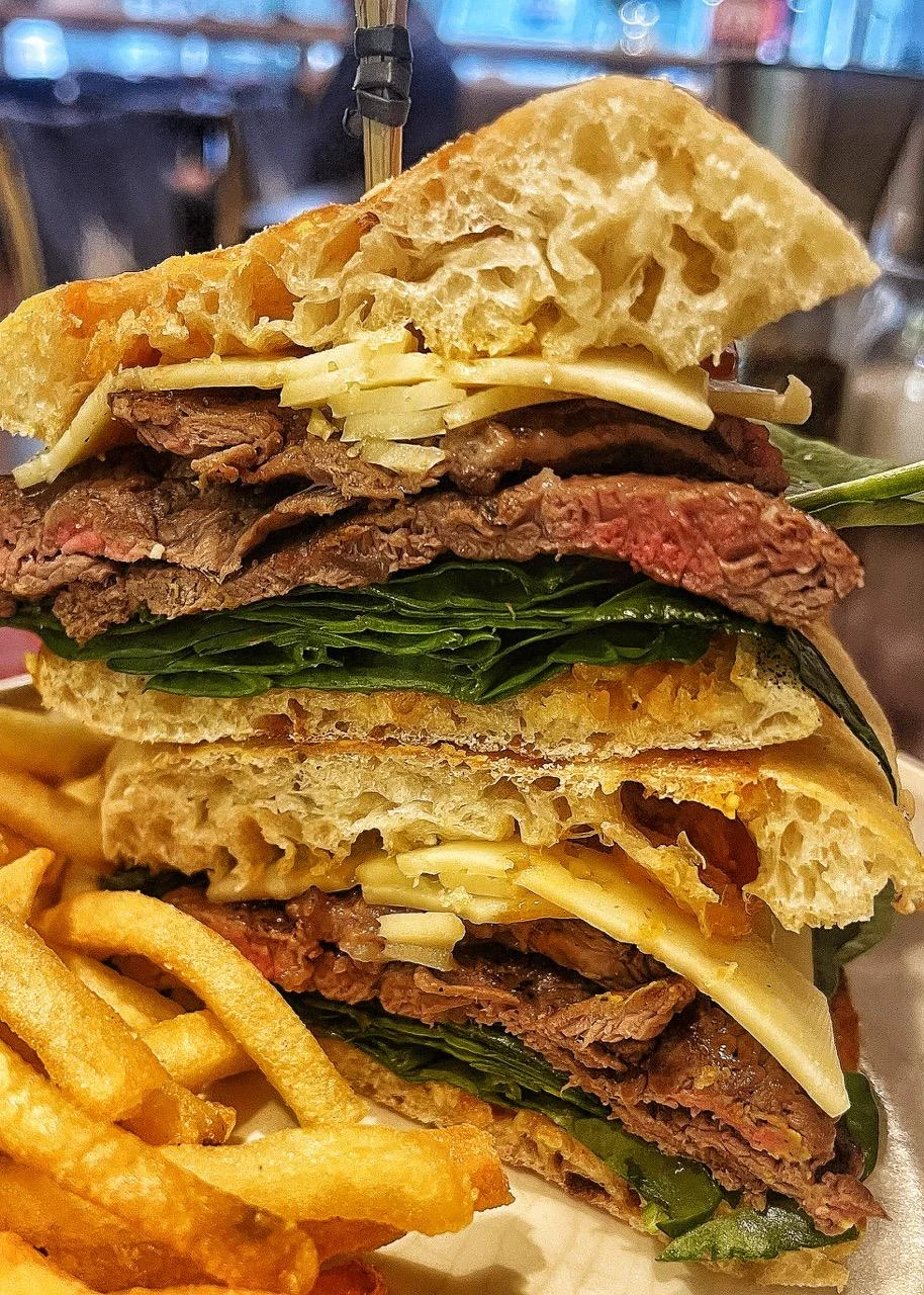 A tall sandwich stacked with layers of roast beef, cheese, and leafy greens, served beside golden fries.