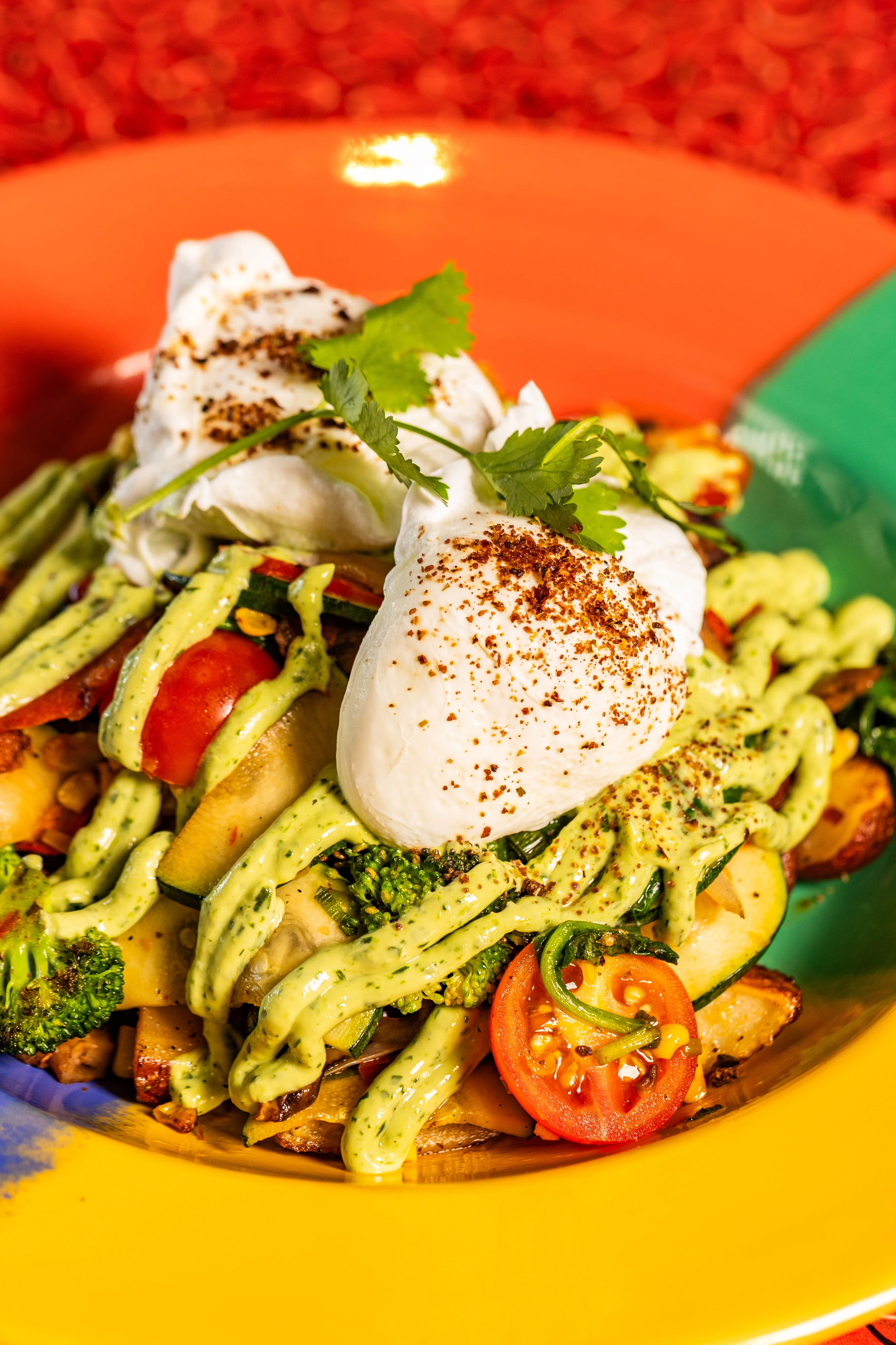 Colorful vegetable brunch bowl with poached eggs and green sauce