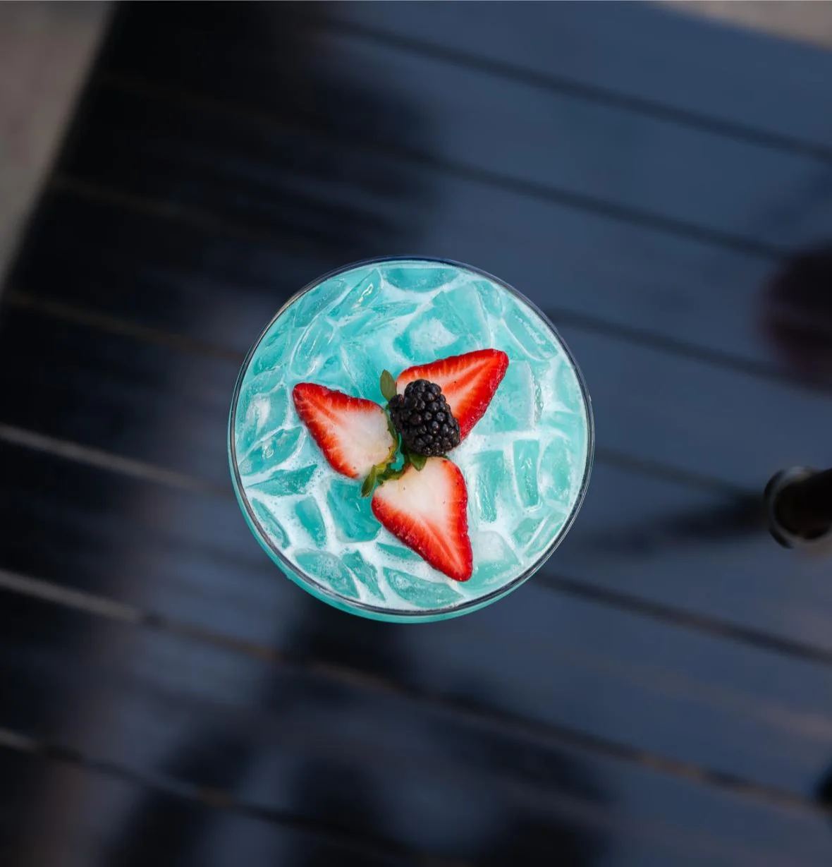 Vibrant blue cocktail garnished with strawberries and blackberries