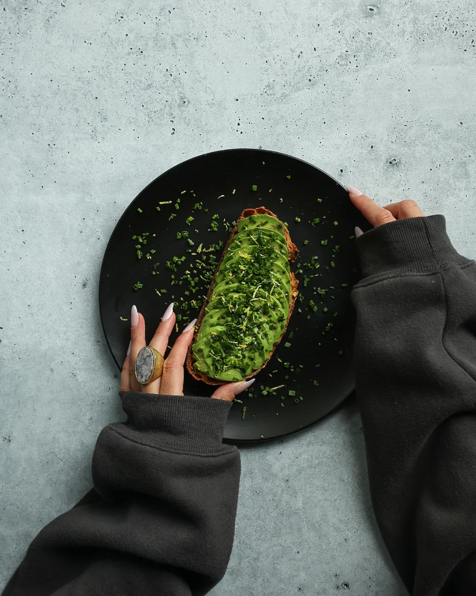 Avocado toast topped with fresh herbs on a black plate