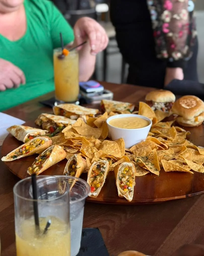 A vibrant spread of appetizers including stuffed tortilla rolls, tortilla chips, and a creamy dip, arranged on a wooden platter.